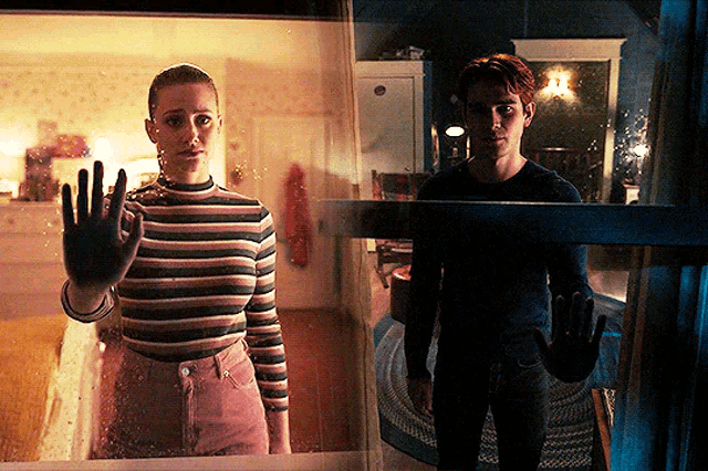 a man and a woman are standing in front of a window and the woman is waving her hand