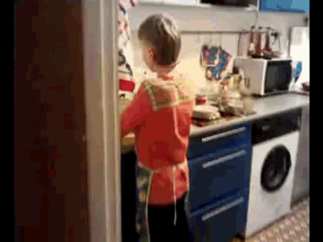 a young boy is standing in a kitchen with a washing machine
