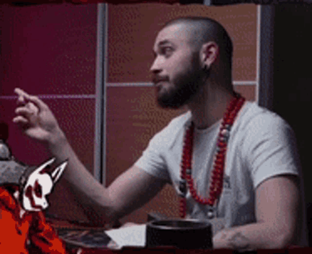 a man with a beard wearing a white shirt and a red necklace
