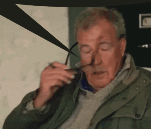 a man in a green jacket is holding a pair of glasses in front of his face