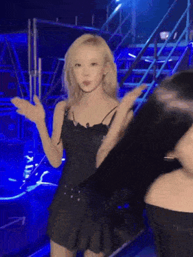 a woman in a black dress is dancing on a stage in front of a blue background .