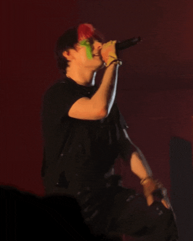 a man in a black shirt is singing into a microphone with green paint on his face