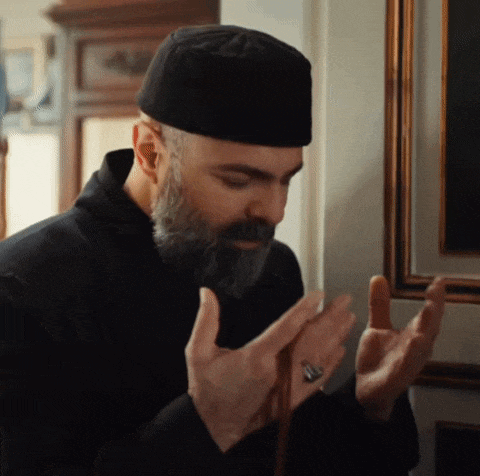 a man with a beard wearing a black hat is praying with his hands together