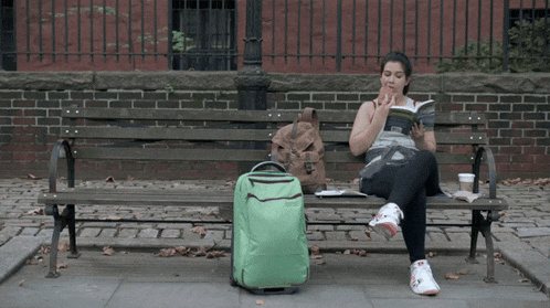 a woman sits on a park bench with a green suitcase