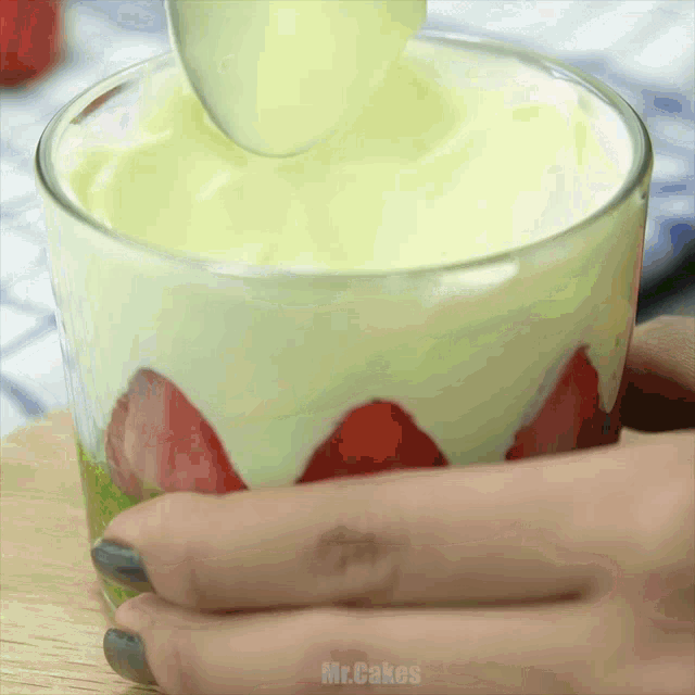 a person is pouring yogurt into a glass with strawberries in it