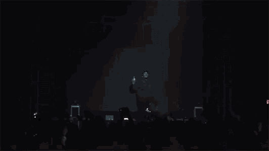 a crowd of people are standing in front of a stage at a concert with their hands in the air .