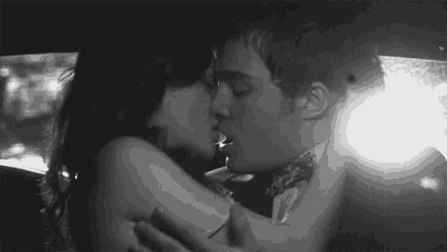 a black and white photo of a man and woman kissing in the back seat of a car .
