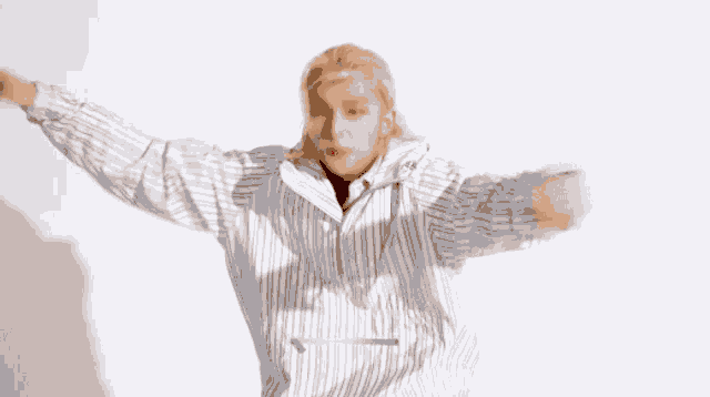 a young man with long blonde hair is wearing a striped shirt and making a funny face .