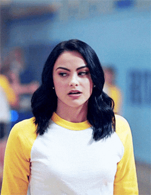a woman wearing a yellow and white baseball shirt looks at the camera