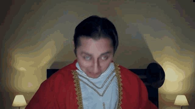 a man in a red robe with gold trim is sitting in front of a bed