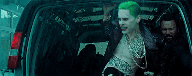 a man in a joker costume is standing in the back of a car .