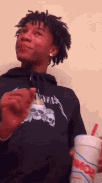 a young man with dreadlocks is holding a cup of soda and a necklace .