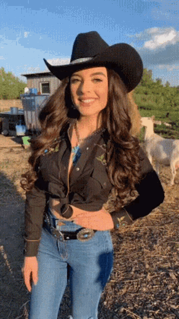 a woman wearing a cowboy hat and jeans is smiling in a field