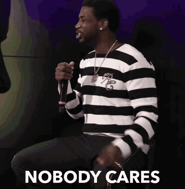 a man in a black and white striped shirt is holding a microphone with the words nobody cares behind him