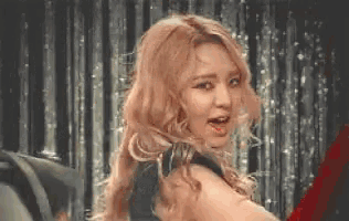 a woman with long blonde hair is standing in front of a curtain .