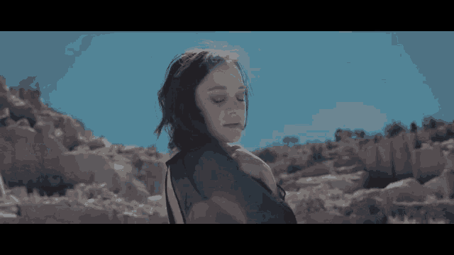 a woman in a black dress is standing on a rocky hillside with her eyes closed .