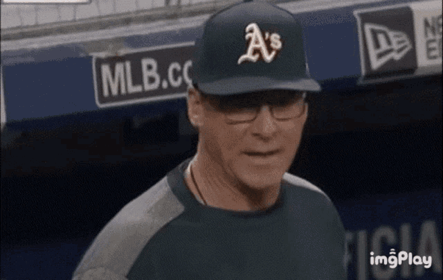 a man wearing a a 's baseball cap and glasses is standing in a dugout .