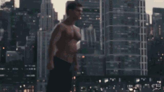 a shirtless man is running through a city in front of tall buildings .