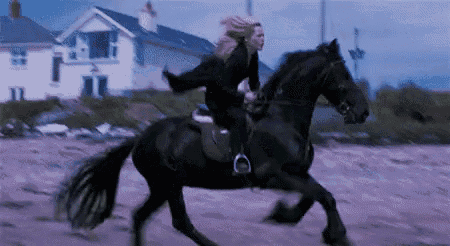 a woman is riding a black horse on a dirt road .