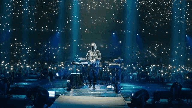 a man playing a keyboard on a stage with a crowd behind him
