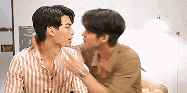 two men are kissing each other in a room while sitting next to each other .