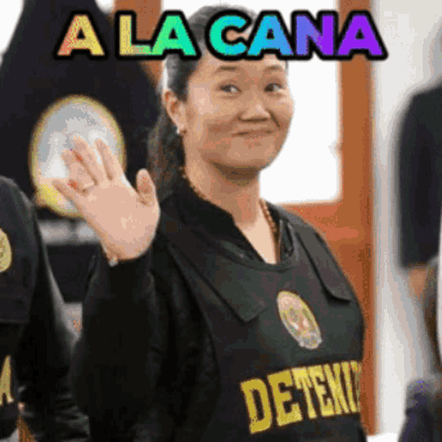 a woman wearing a black shirt that says " deteni " is smiling and waving