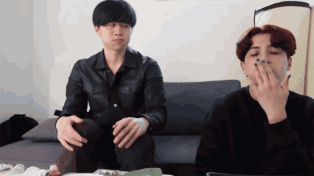 two young men are sitting on a couch one has a bandage on his arm