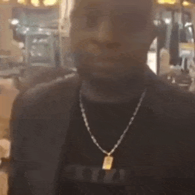 a man wearing a black shirt and a gold chain is standing in a gym .
