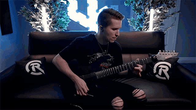 a man playing a guitar on a couch with a wall of fame logo in the background