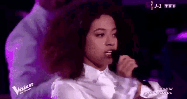 a woman with curly hair is singing into a microphone on stage .