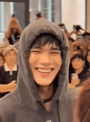 a man wearing a hooded sweatshirt is smiling in front of a crowd of people .