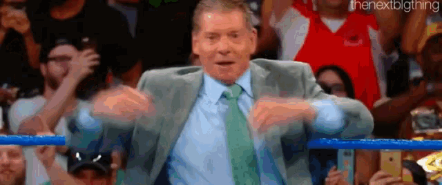 a man in a suit and tie is standing in a wrestling ring with his hands in the air .