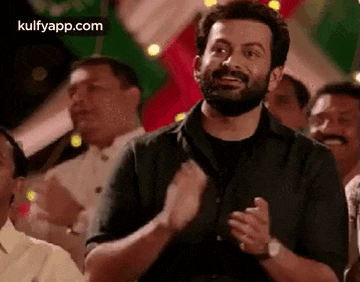 a man with a beard is clapping in a crowd of people .