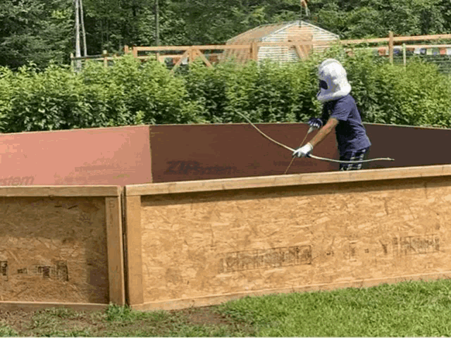 a man wearing a mask sprays a wooden fence with zipsystem
