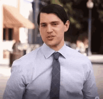a man in a blue shirt and tie is standing on a street .