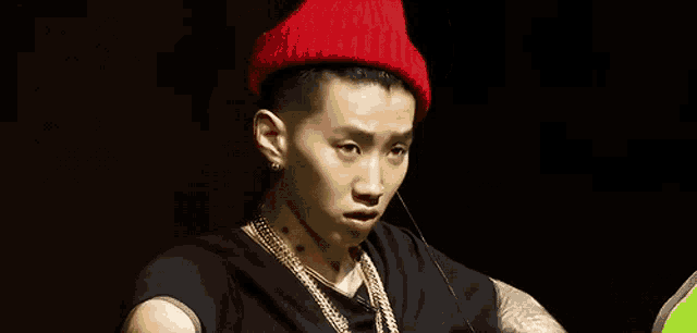 a young man wearing a red hat and a black shirt is looking at the camera .