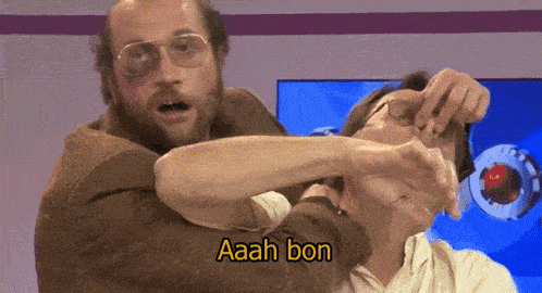 a man with glasses is holding another man 's face and says aaah bon on the bottom