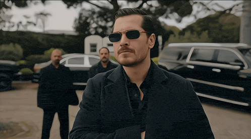 a man wearing sunglasses stands in front of a car