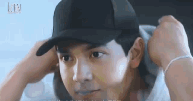 a man wearing a black hat and a white shirt is looking at the camera .