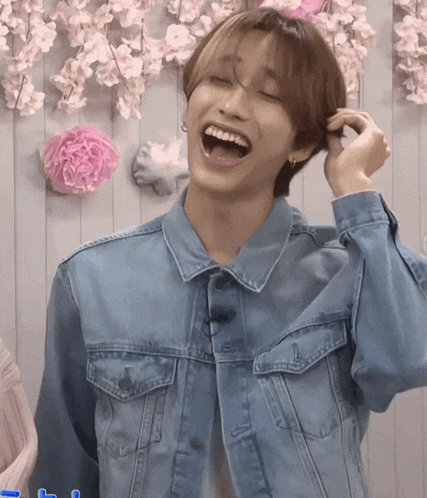 a young man in a denim jacket is laughing with his mouth open