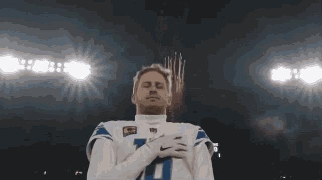 a football player is standing on a field with his eyes closed and his hands on his chest .