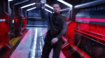 a man with a beard is dancing in a futuristic hallway with red lights .
