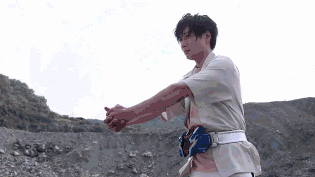 a man in a white shirt with a blue belt around his waist is standing in a rocky area