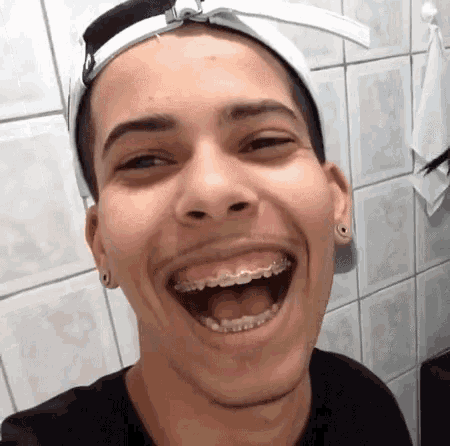 a young man with braces on his teeth is laughing while wearing a hat .