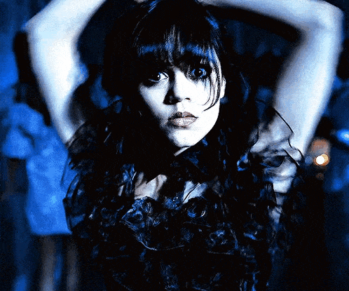 a woman in a dark blue dress holds her hands behind her head
