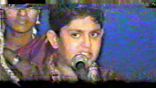a young boy singing into a microphone with a blurry background behind him