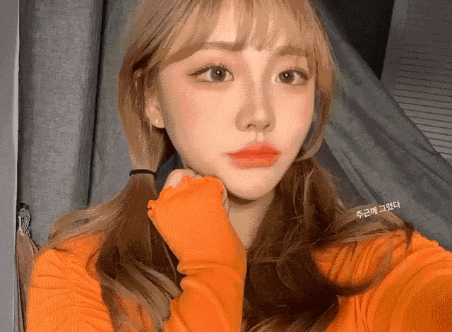 a girl with blonde hair is wearing a bright orange sweater