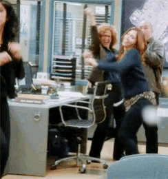 a group of people are dancing in a room with a desk and chairs