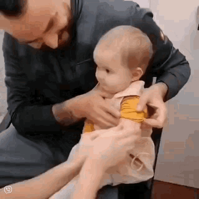 a man is putting a yellow shirt on a baby 's arm .