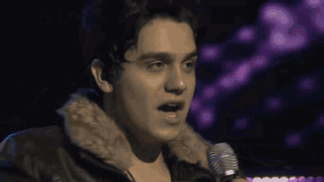 a man singing into a microphone in front of a purple background